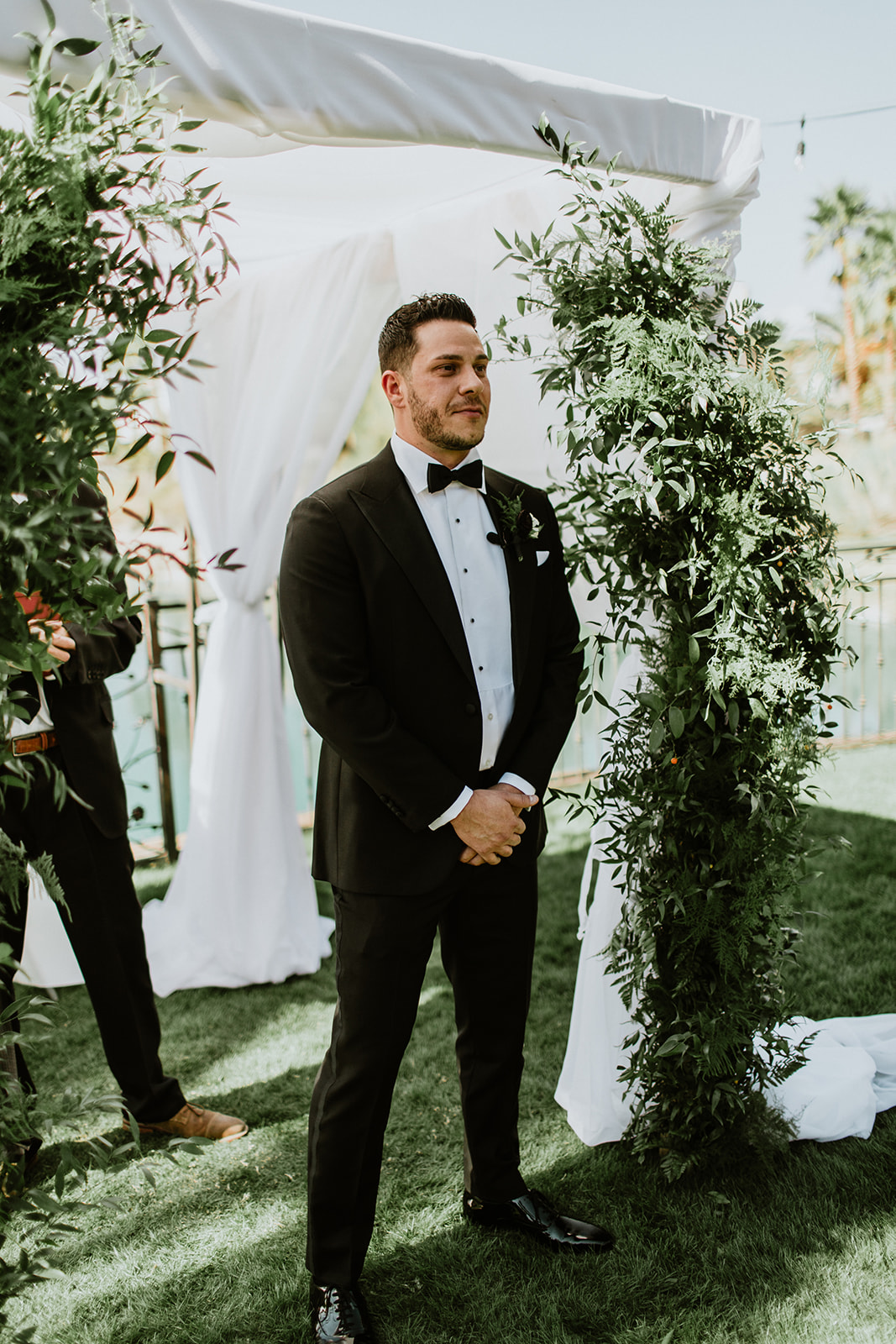 Groom waiting under chuppah with greenery for bride 