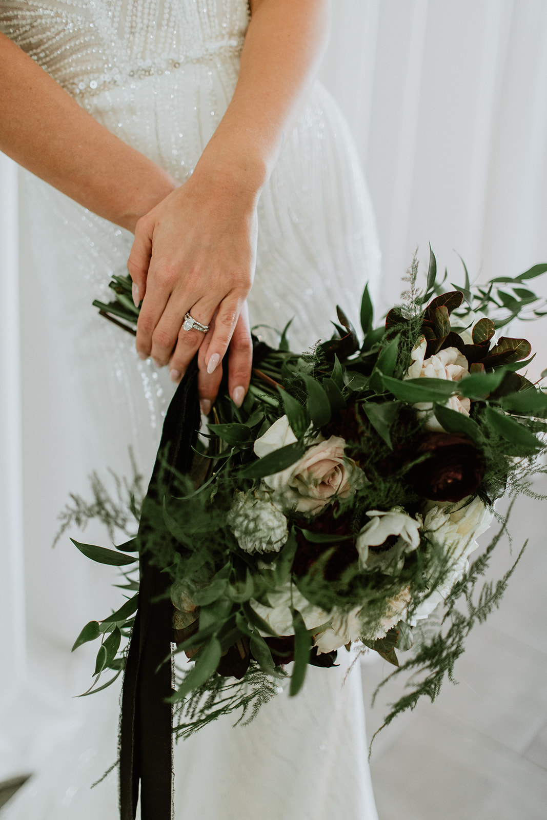 Brides hands with Wedding Ring holding lush green white and black  bouquet 