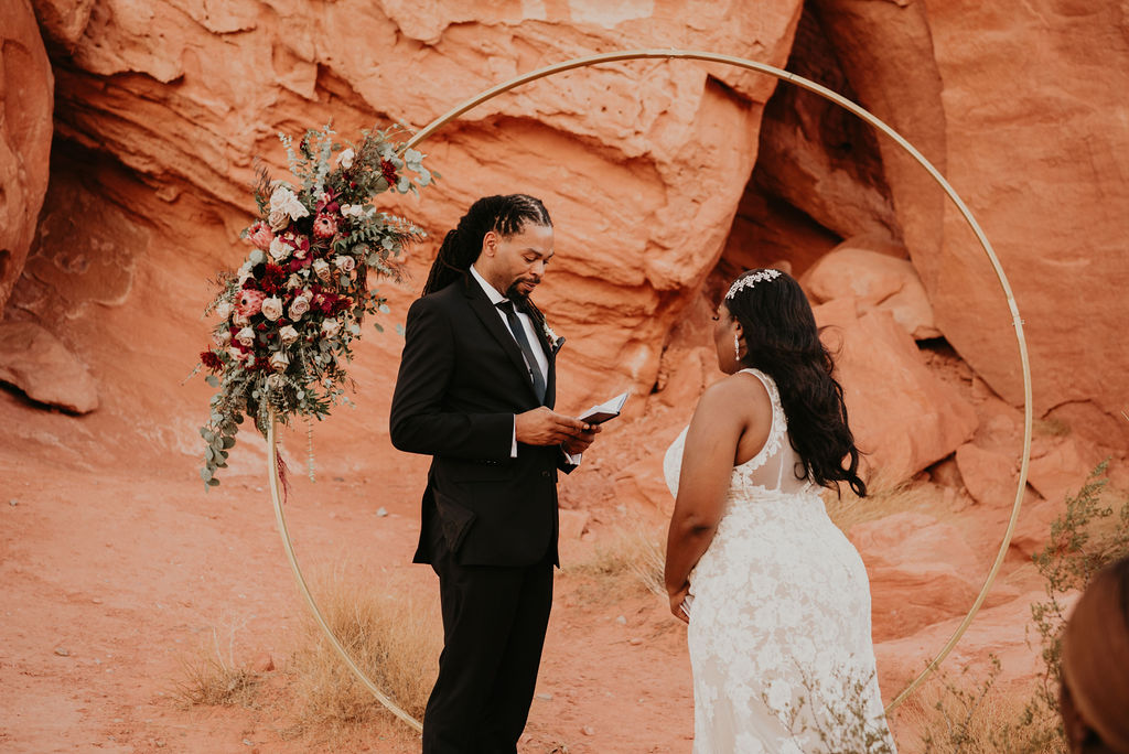 Groom Reading Vows to Bride During Ceremony in front of Circle Arch for Rustic Pink Burgundy and Sage Elopement 