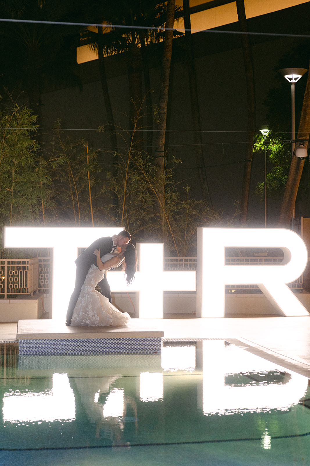 Bride and groom kissing in front of lights with their initials at Red Rock Casino pool 