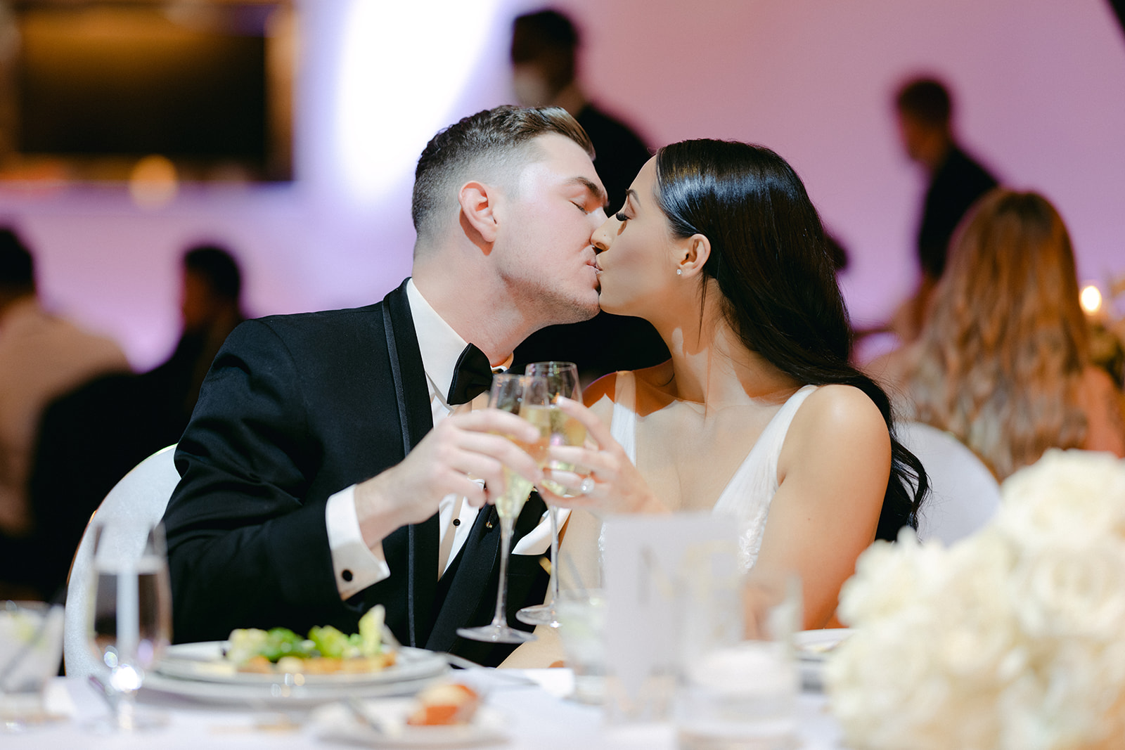 Bride and groom drinking champagne and kissing during reception 