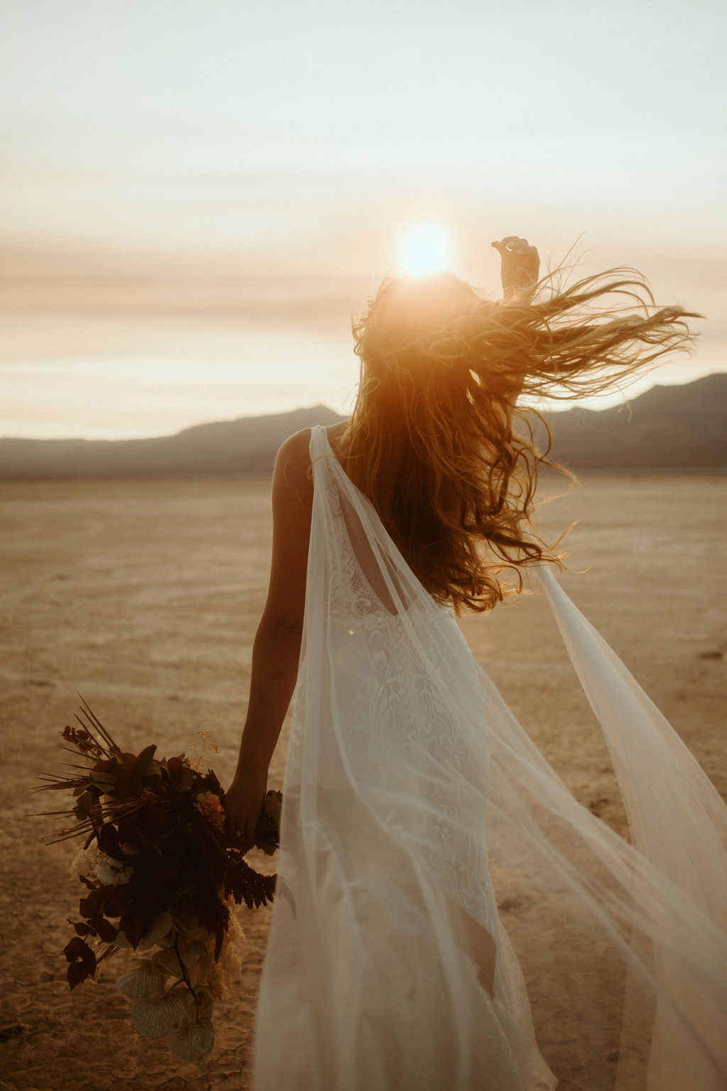 Bride wearing Bridal Cape Playing with Hair Blowing in Desert Wind 