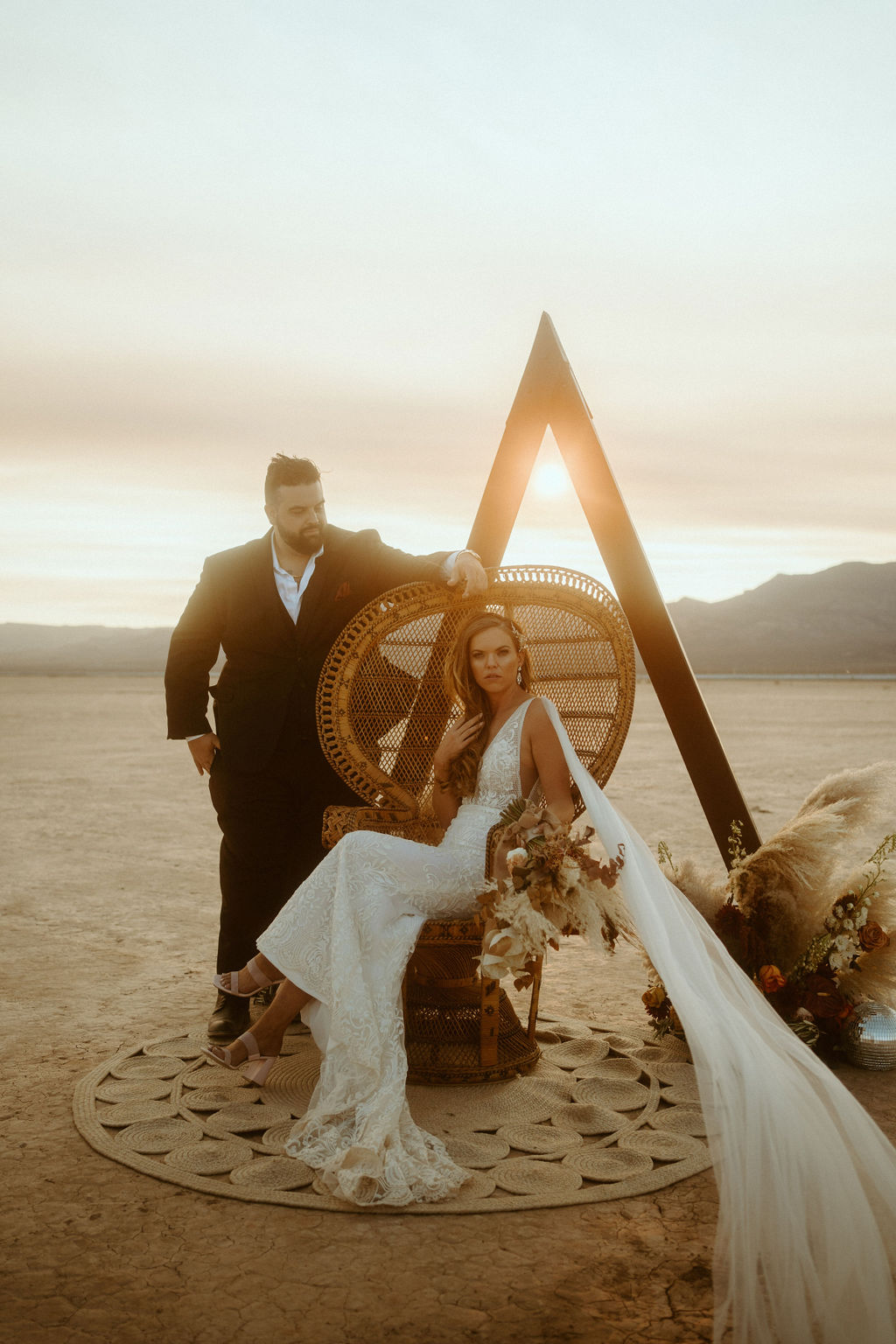 Bride Sitting on Peacock Chair by Triangle Arch and Boho Rug during Sun Set at Retro Disco Bohemian Micro-Wedding