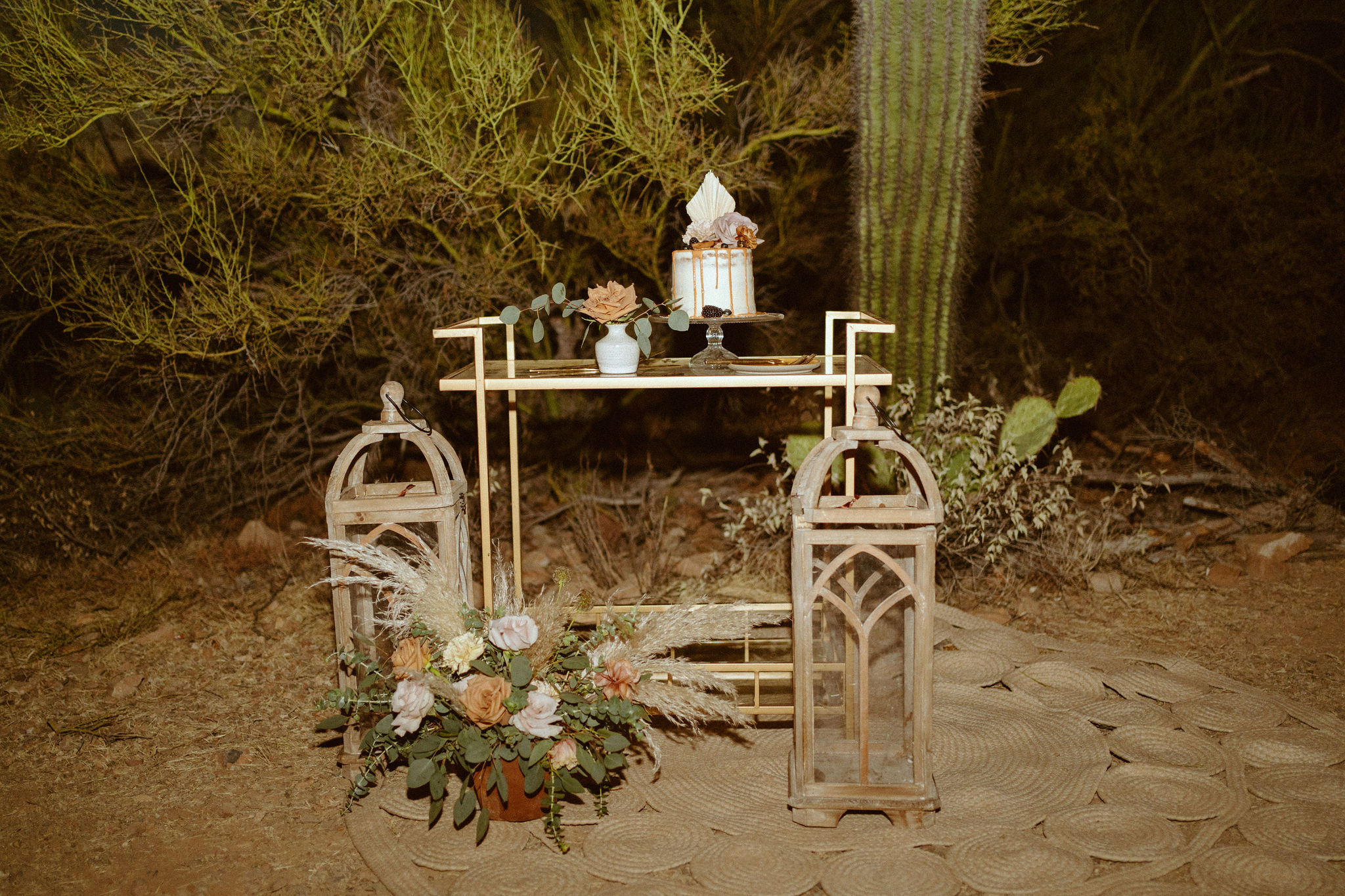 Bar cart cake table in front of the cactus with wooden lanterns and florals 
