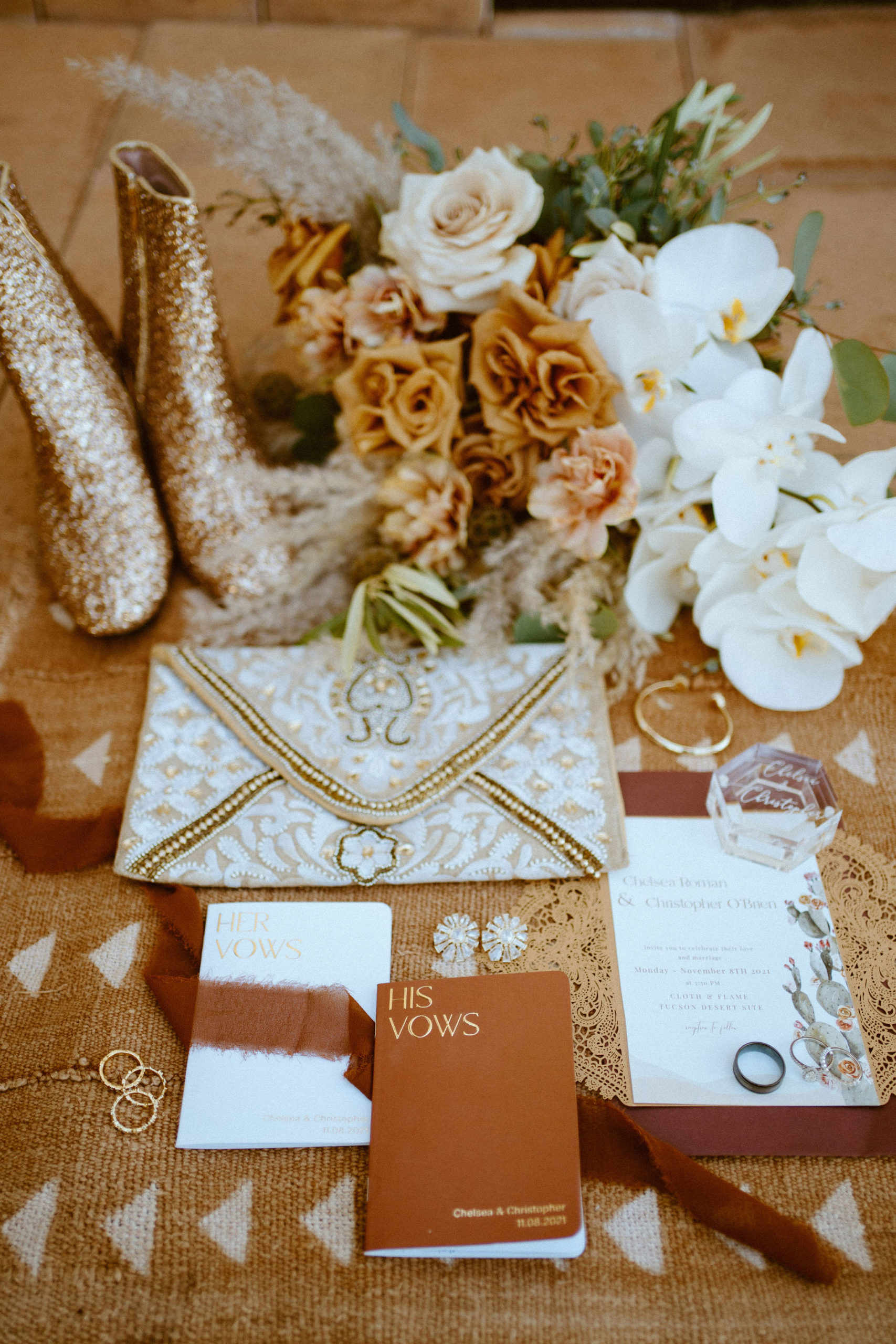 Saguaro National Park Micro-Wedding. Detail photo of the brides wedding shoes, the invitation suite, the bride and grooms rings, the brides bracelet and wedding day clutch with vow books and the brides bouquet.