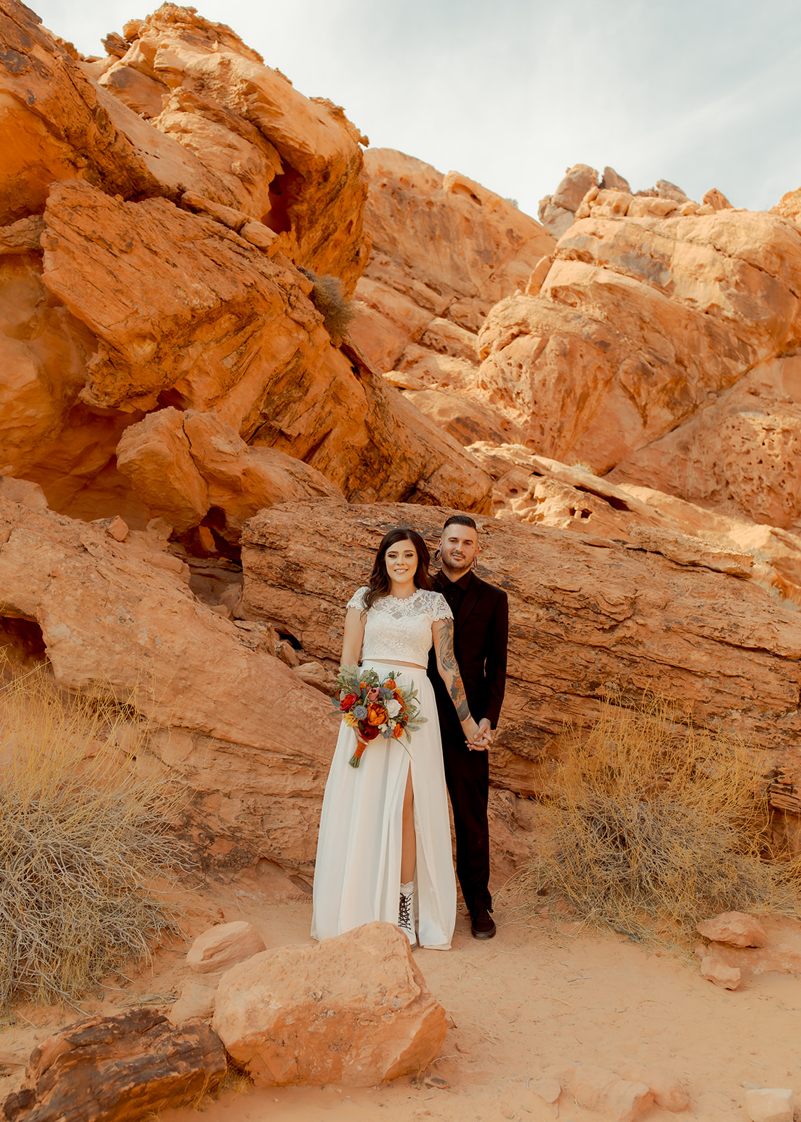 Groom in all black suit and bride in two piece bridal dress holding hands after eloping in Nevada 
