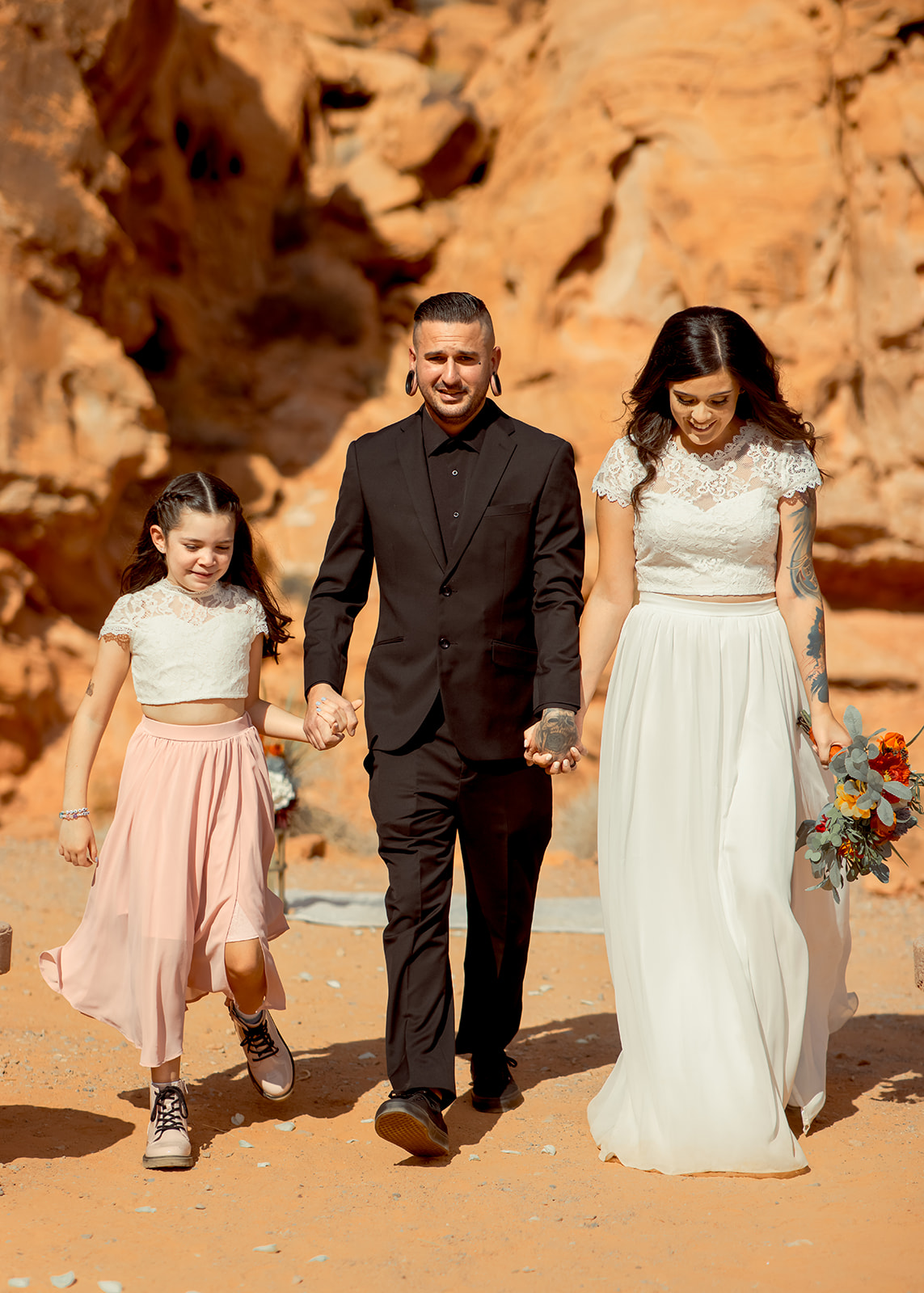 Groom in all black and bride in two piece wedding dress exits ceremony with Daughter at Valley of Fire Rock N Roll Wedding