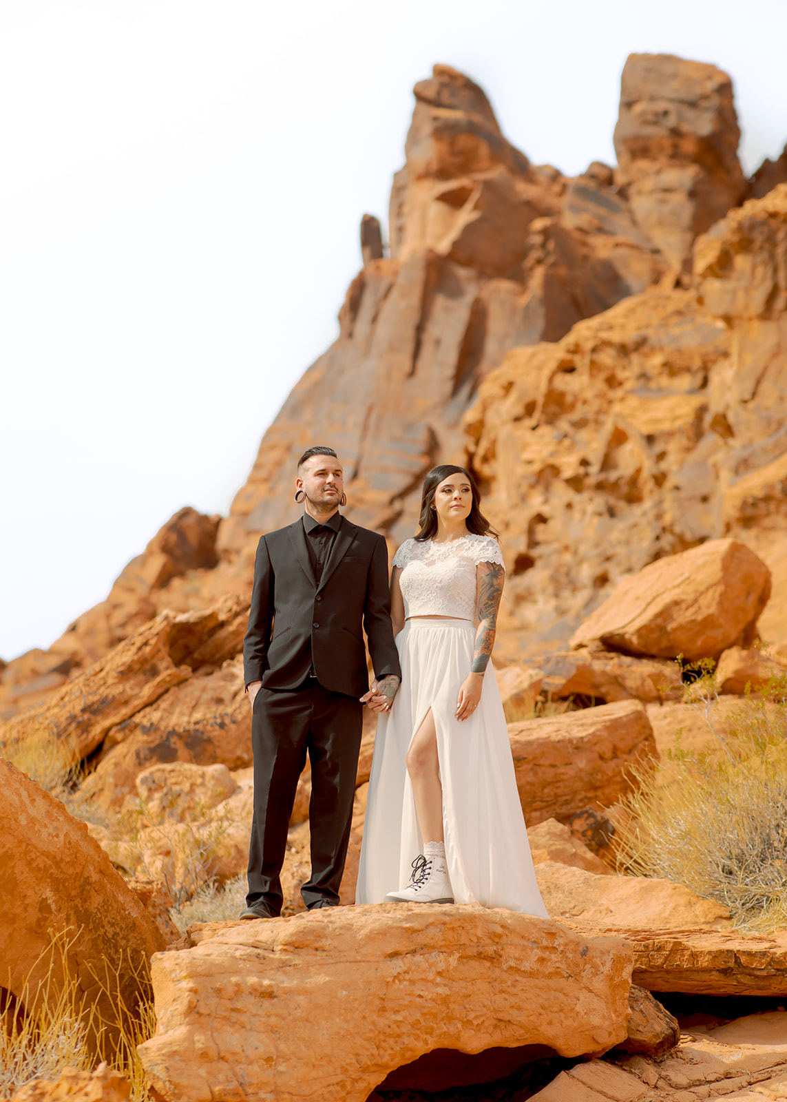 Groom in all black suit and bride in two piece dress standing on dramatic red rocks at Valley of Fire 