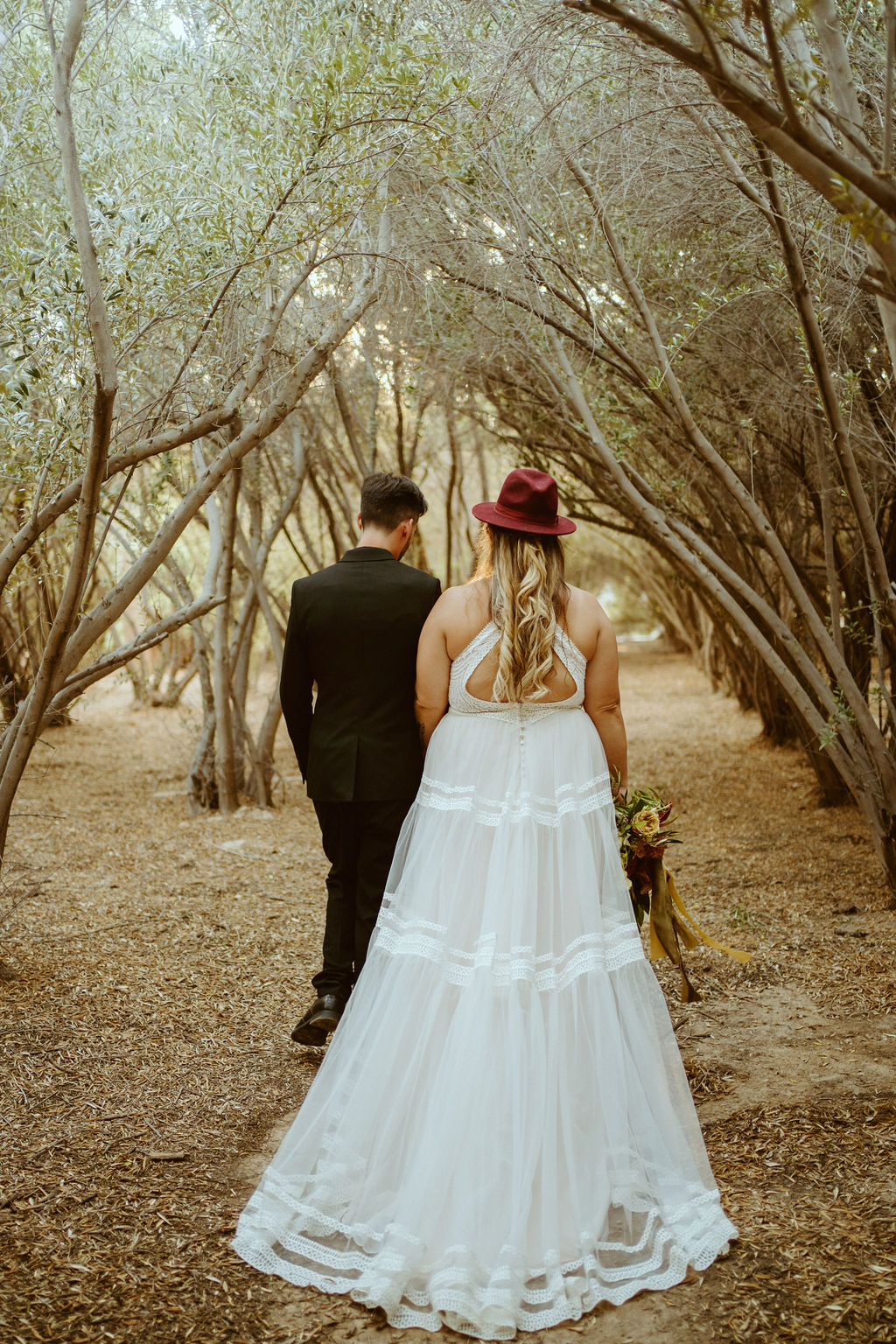 Bride in Hat walking with groom in olive grove 
