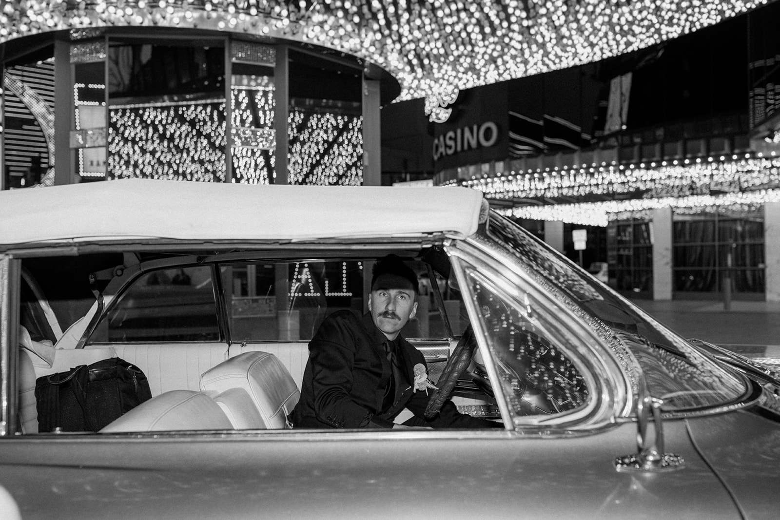 Black and White Photo of Groom Parking Classic Car in Downtown Las Vegas Hotel after Modern Retro Wedding 