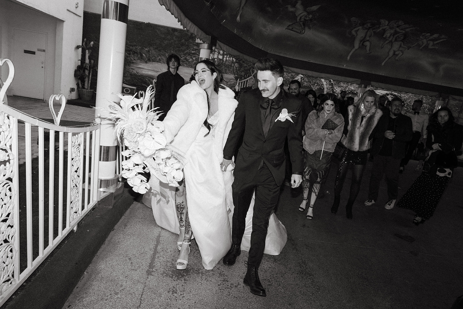 Black and White Photo of Bride in White Fur Coat Exiting Vegas Ceremony 
