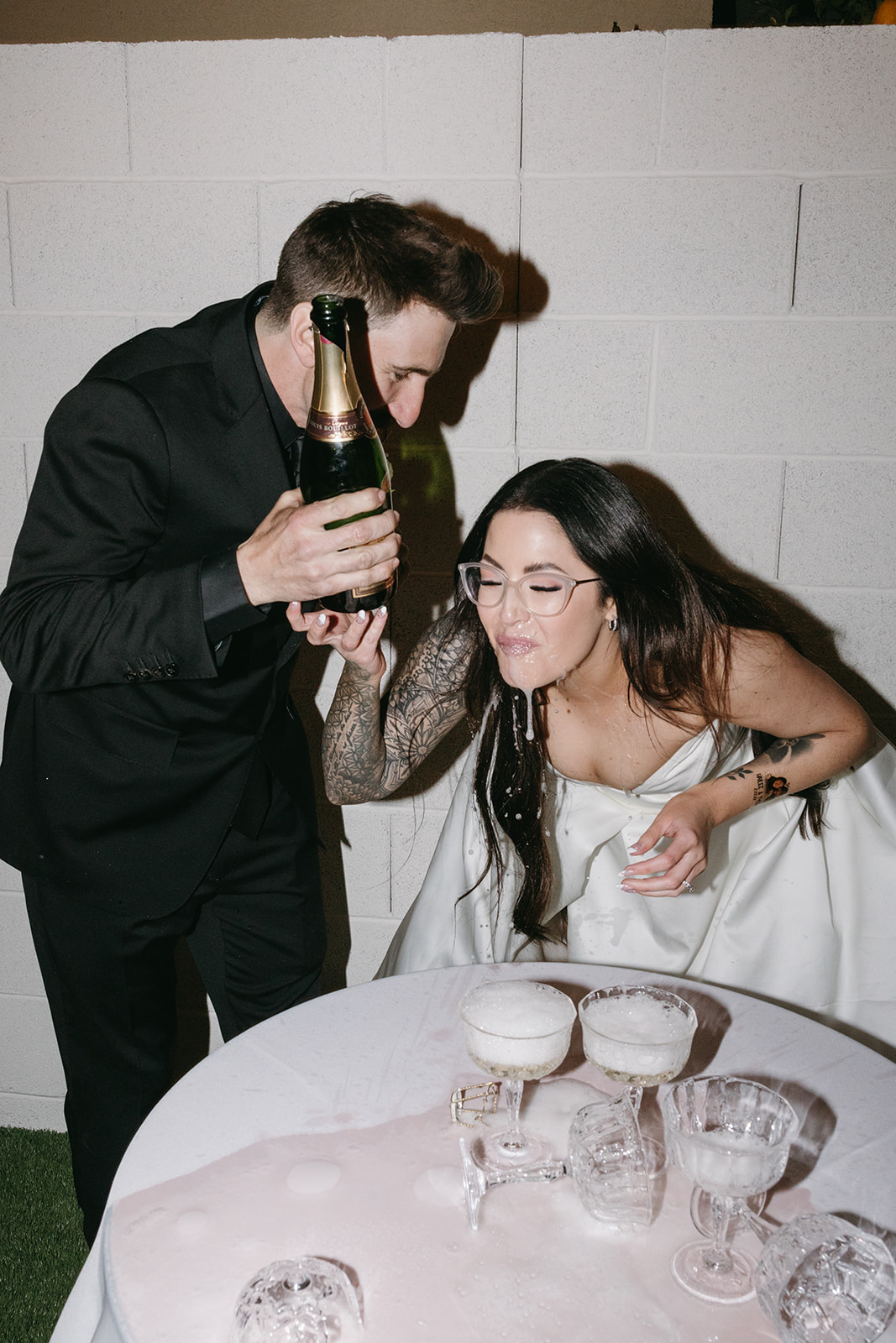 Newlyweds spilling Champagne after Champagne glass tower spill during their fun Vegas backyard reception dinner 