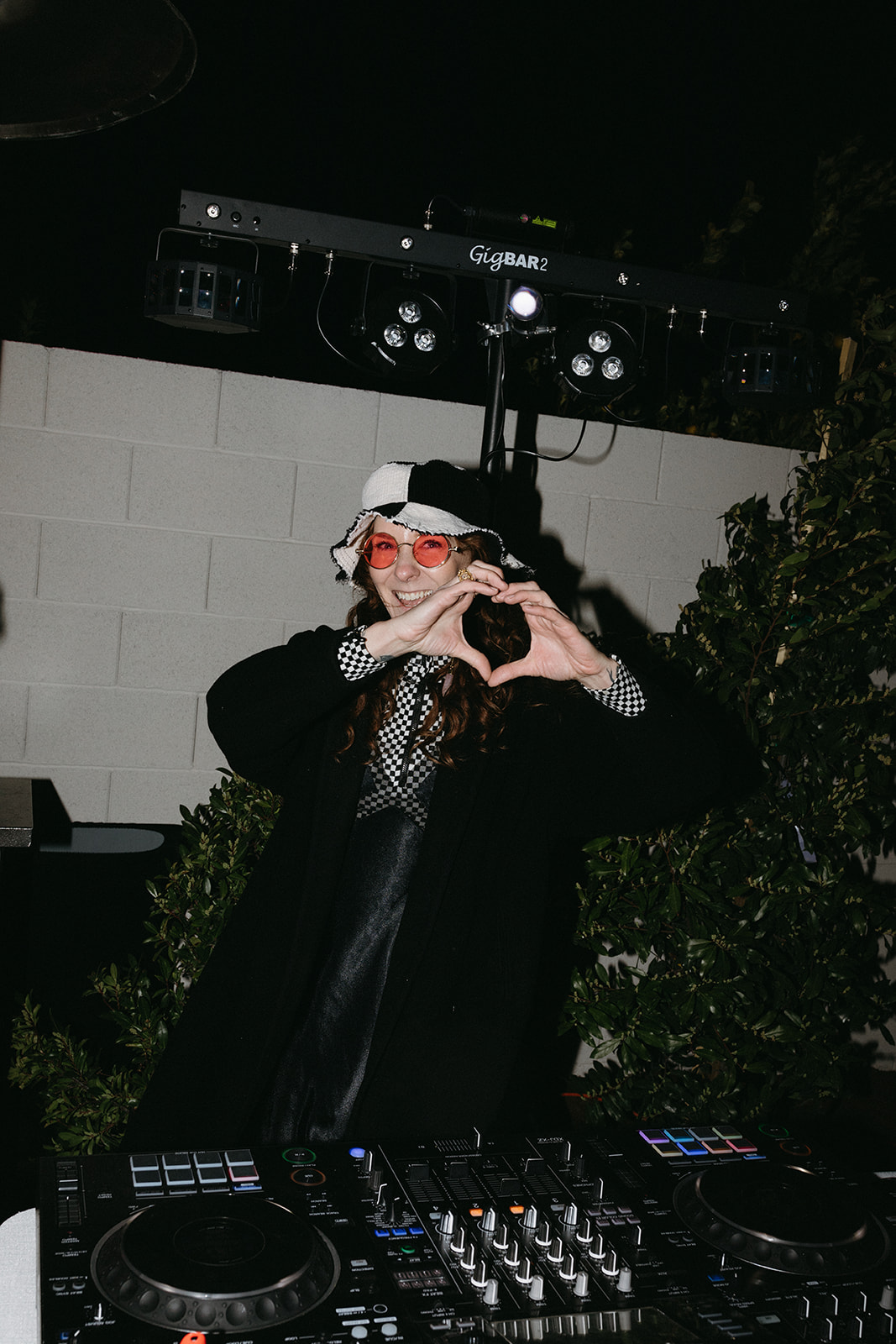 DJ making Heart with her Hands while wearing red party favor glasses and being DJ for Modern Retro Wedding Reception 