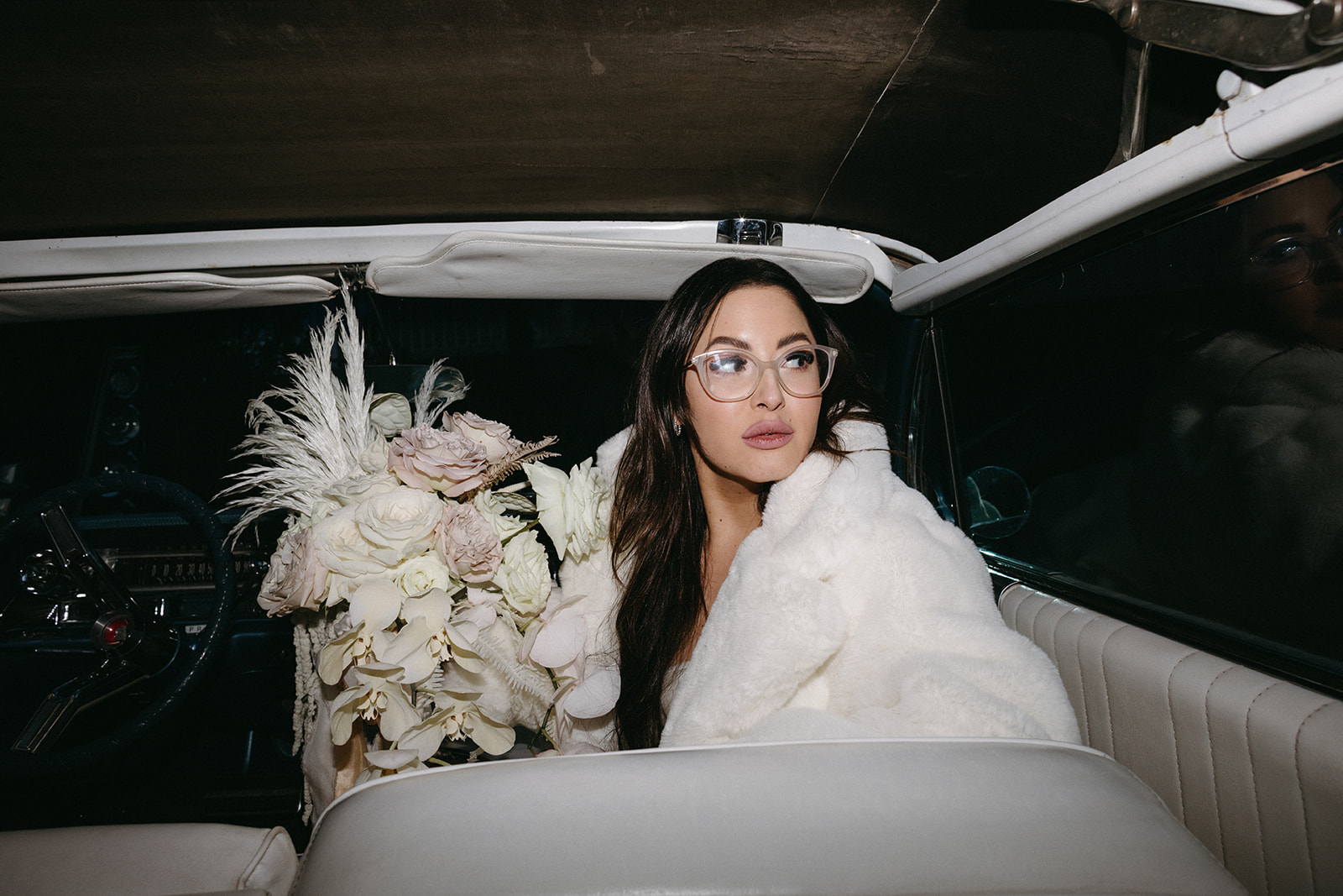 Bride in Classic Car and White Fur Coat holding Modern Bouquet 