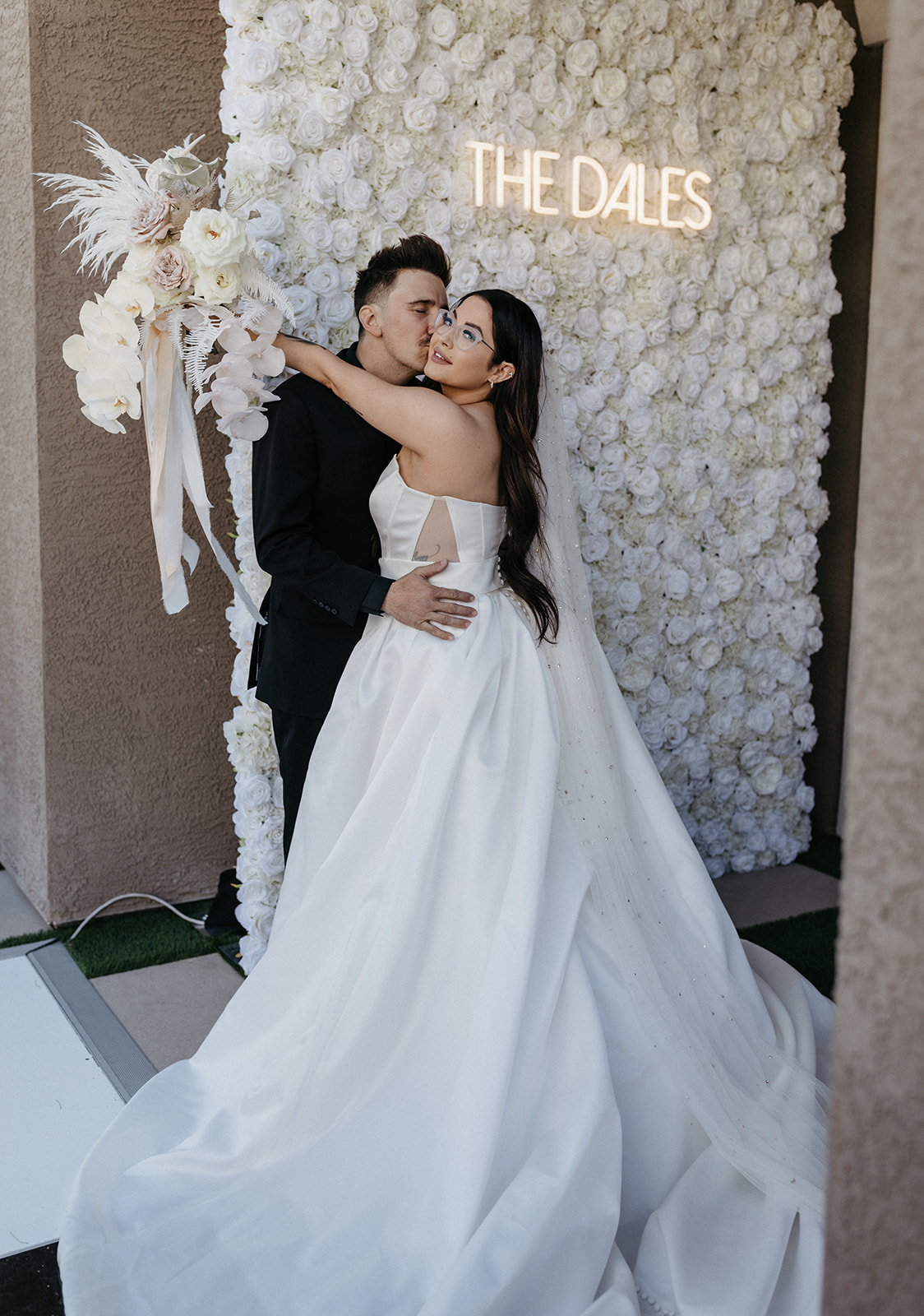 Newlyweds with Neon Sign, White Flower Wall, & Bouquet for Little White Wedding Chapel Modern Vegas Wedding