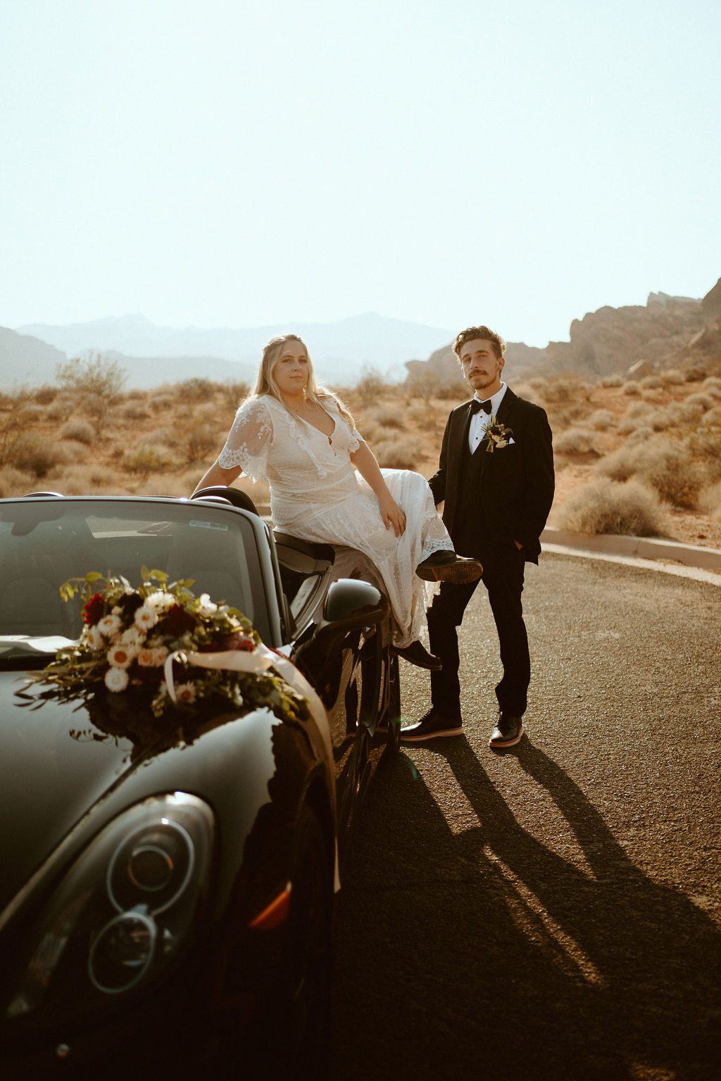 bride and groom sitting on car after eloping 
