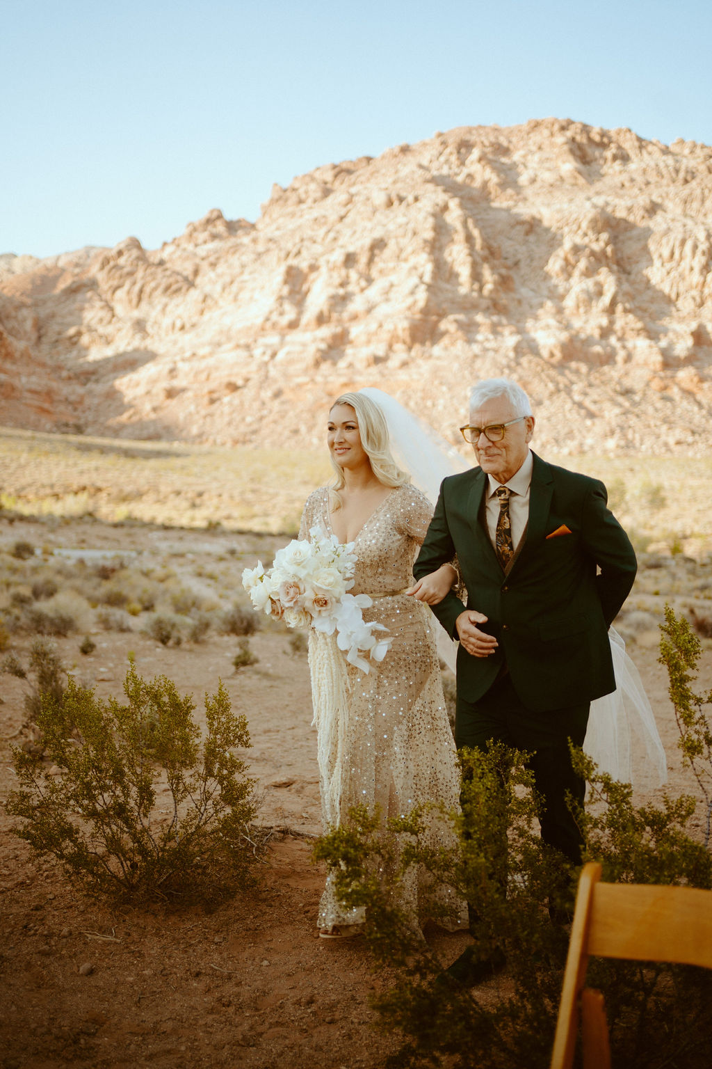 The bride accompanied by her father walking down the desert aisle. 