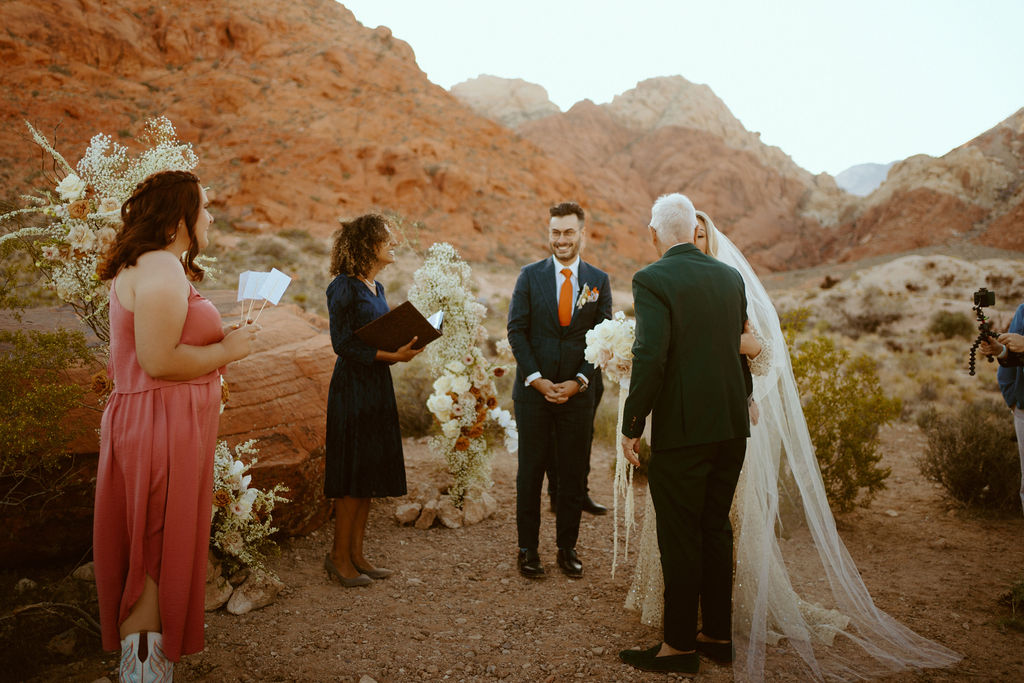 Father of the bride giving his blessing to give the bride to the groom at the altar in front of the red rocks of ash springs. 