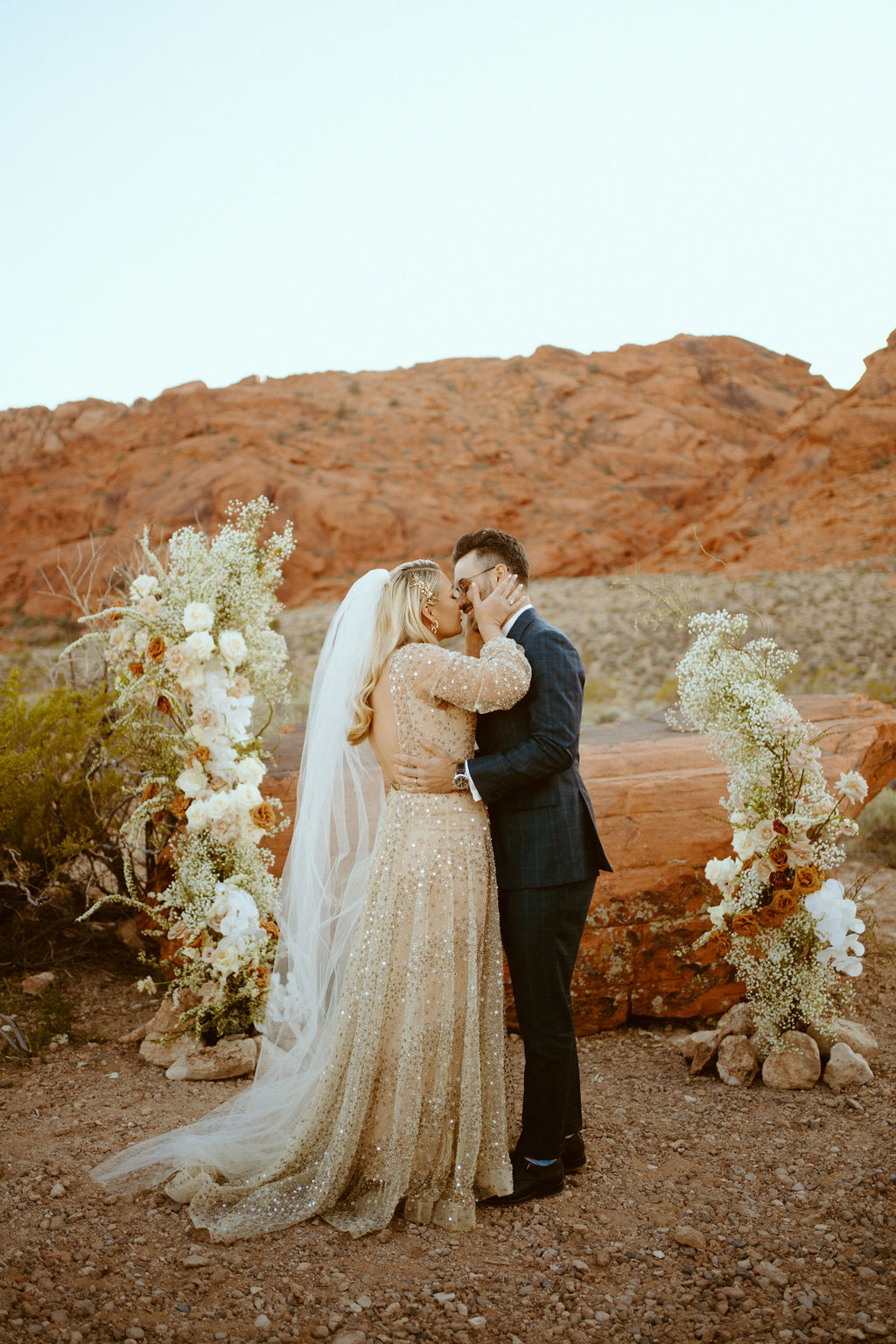 Micro-Wedding Reception at Ash Springs. The first kiss as Mr. & Mrs. in between the asymmetrical floral arch in front of the red sandstone rocks.