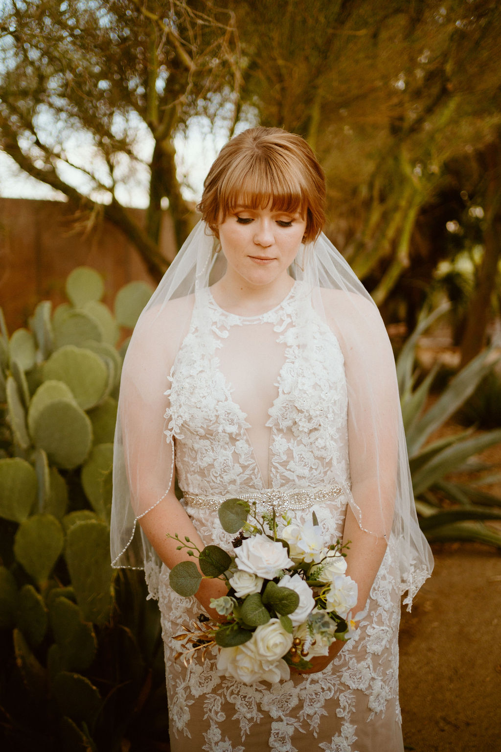 Bride with detailed lace dress and white rose bouquet with greenery 