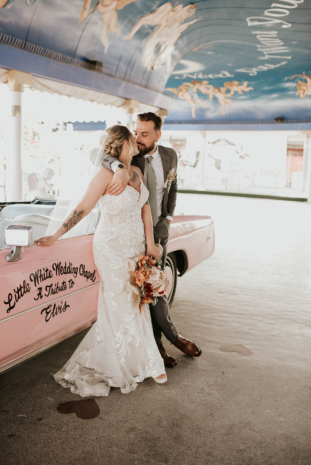 Bride and groom lean on the pink Cadillac sharing a kiss. 
