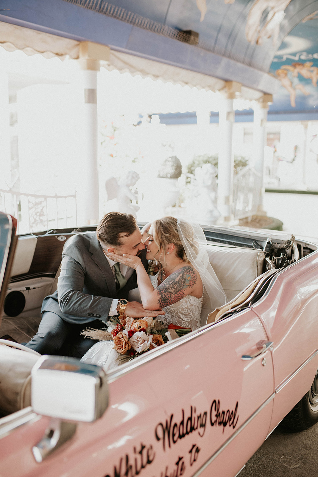 Bride smiles caressing her new husbands face inside the pink Cadillac. 