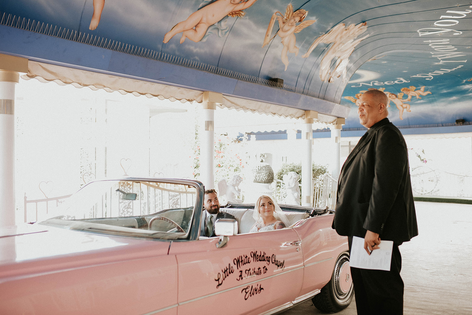 Officiant standing outside of the Pink Cadillac while the bride and groom sit inside to be married. 