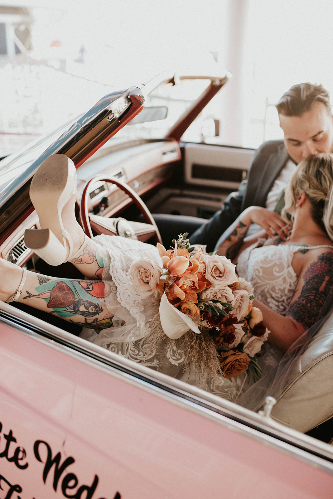 First Stop! A Little White Chapel Bride hangs her feet out of the cute pink Cadillac leaning into her husband. The bride is wearing cute chunky white heals