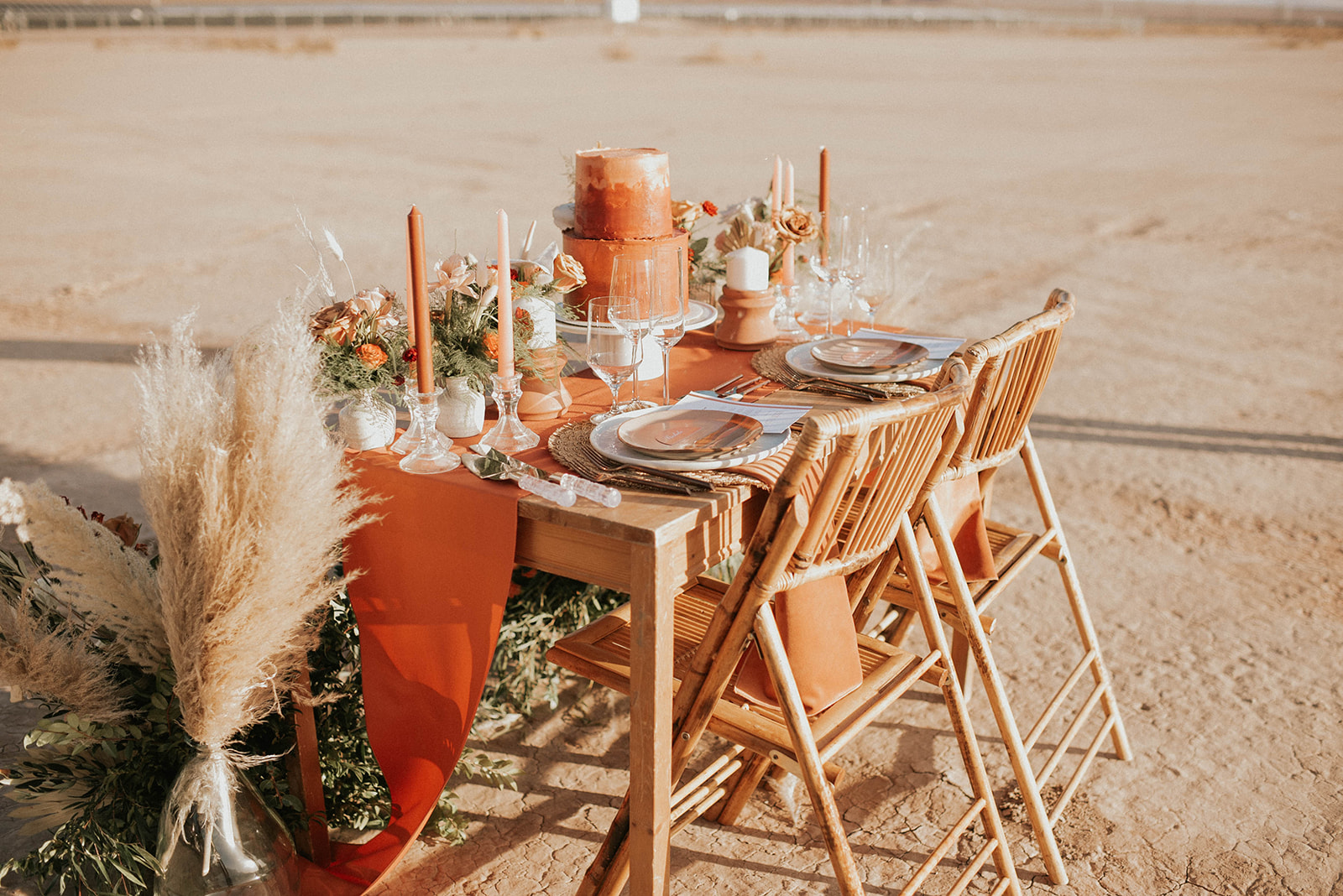 Boho styled sweetheart table with pampas candles and wooden chairs. Burnt orange table runner with whicker wooden chairs. 
