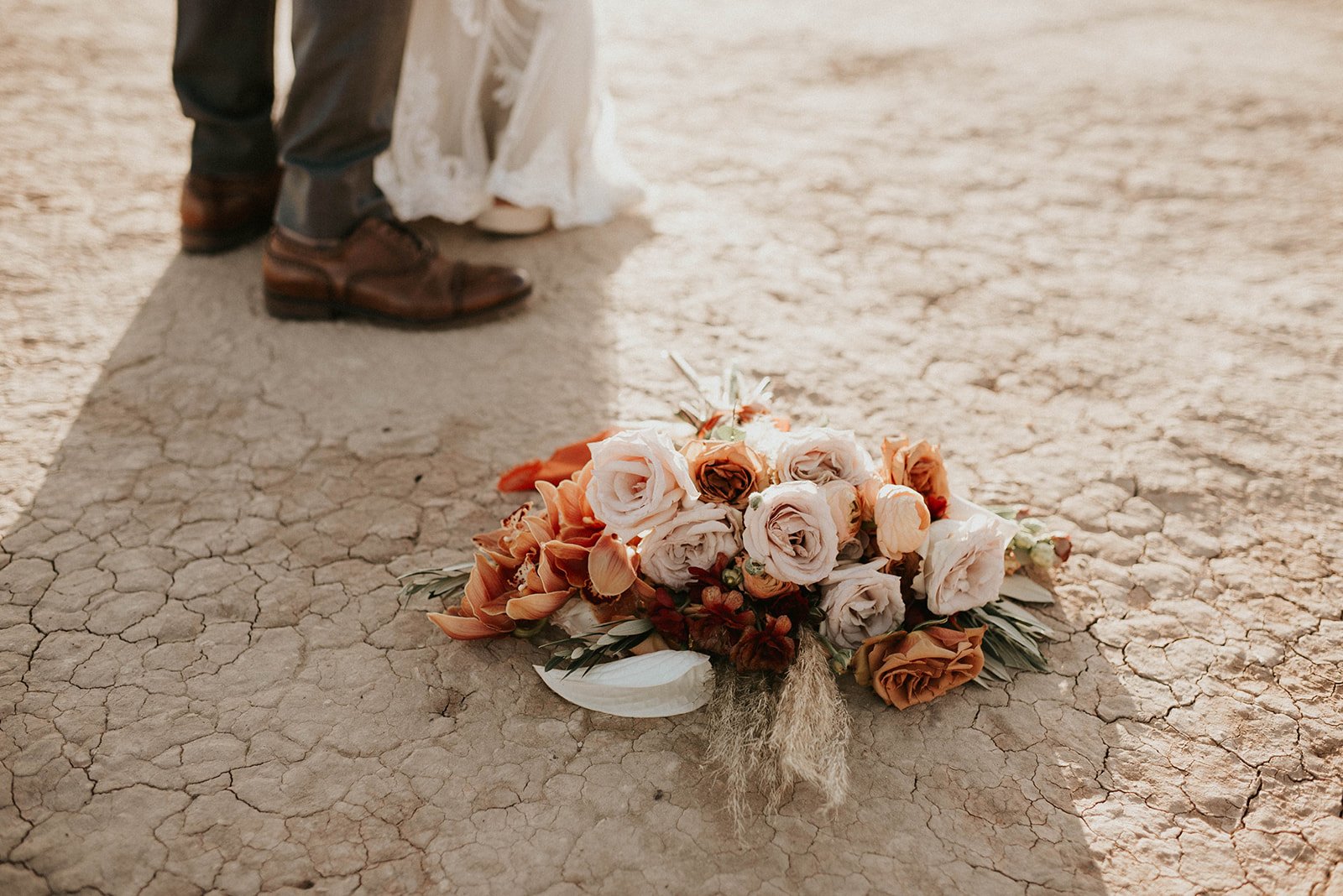 First Stop! A Little White Chapel brides bouquet laying on the desert floor. Bride and grooms shoes out of focus in the background. 
