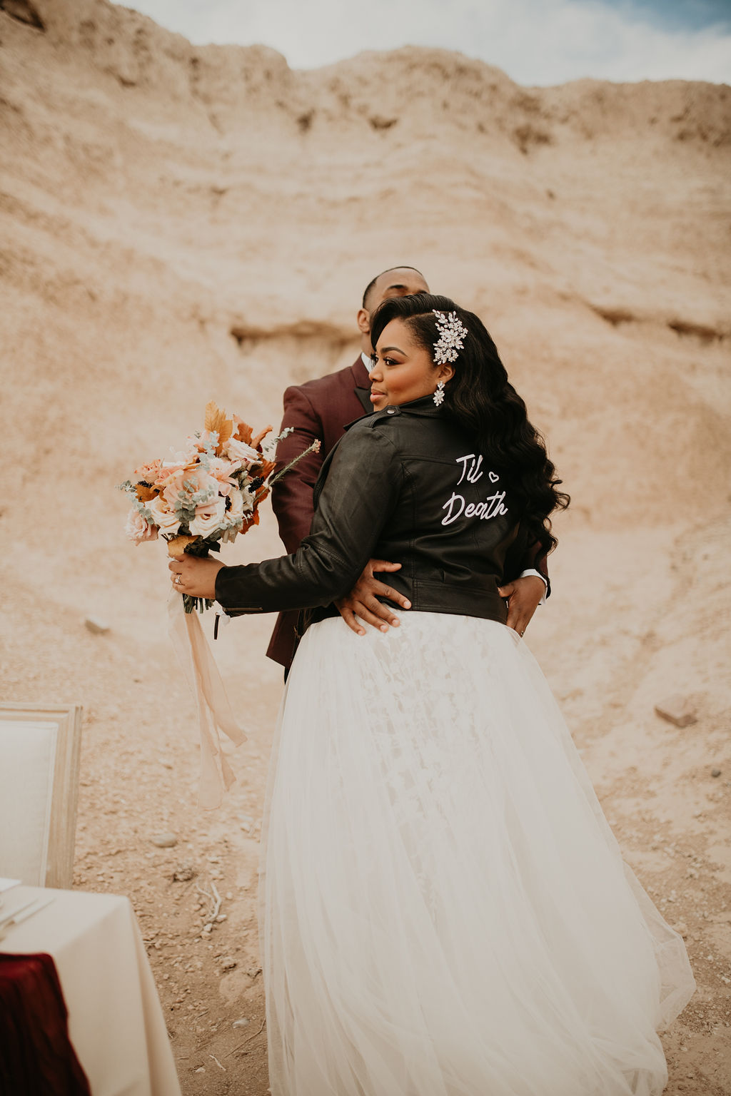 Fossil Beds Sunset Elopement. The beautiful bride sporting a custom leather wedding jacket saying "till death" as her and the groom face each other 