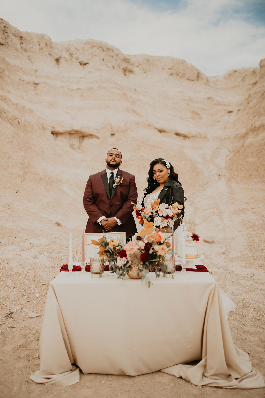 Fossil Beds Sunset Elopement newlyweds standing behind the sweetheart table that's covered in a gold linen and a burgundy runner with taper and votive candles placed all around. 