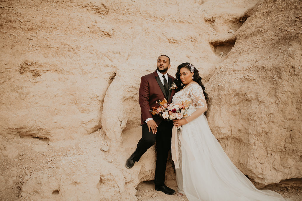 Bride and groom standing next to the large ash rocks in fossil beds. The groom has his foot placed on the rock as the bride leans in on him. 