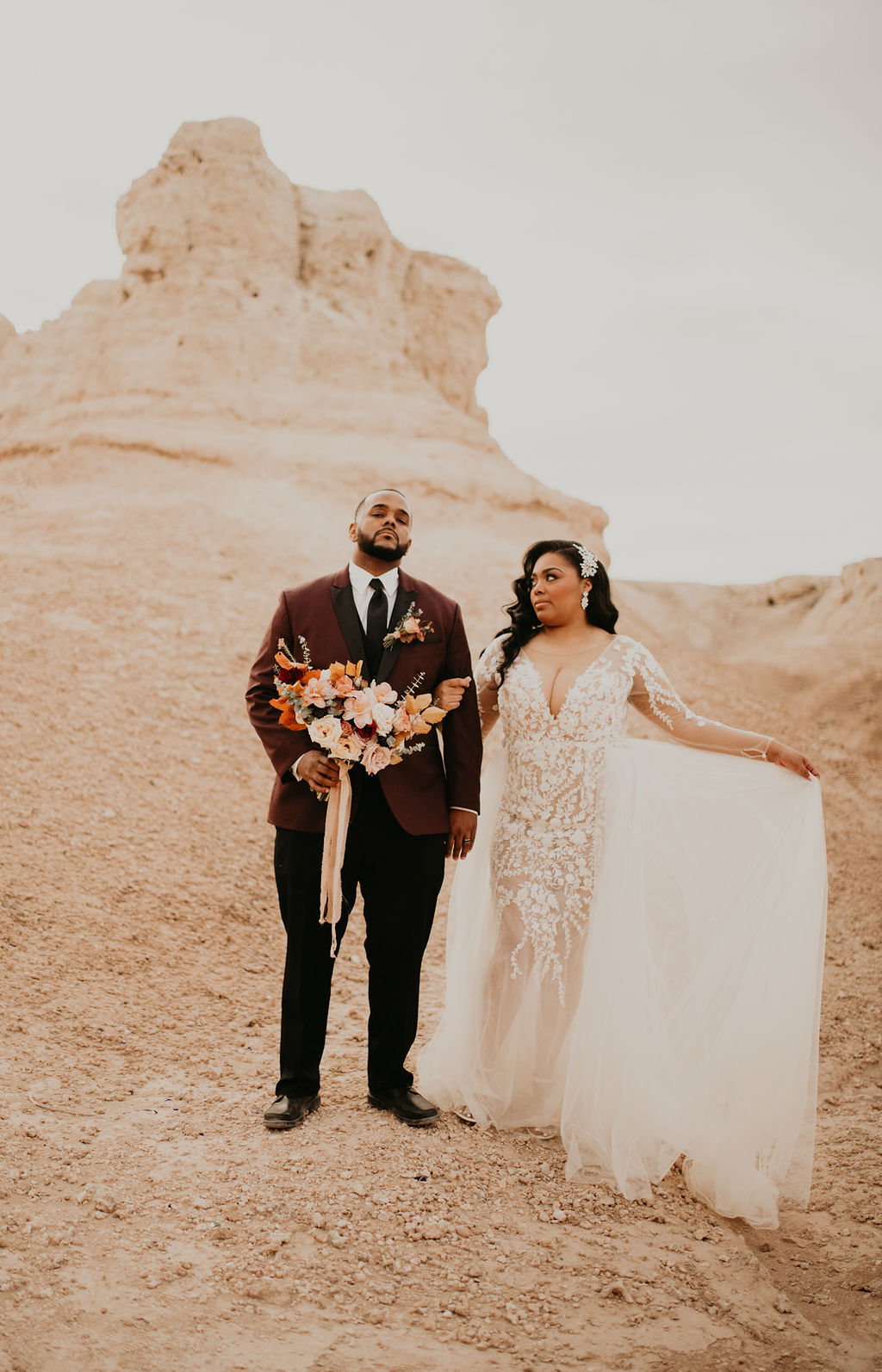 The beautiful bride holding out the tule of her wedding dress while holding the groom in front of the rocks in the desert of the fossil beds. 