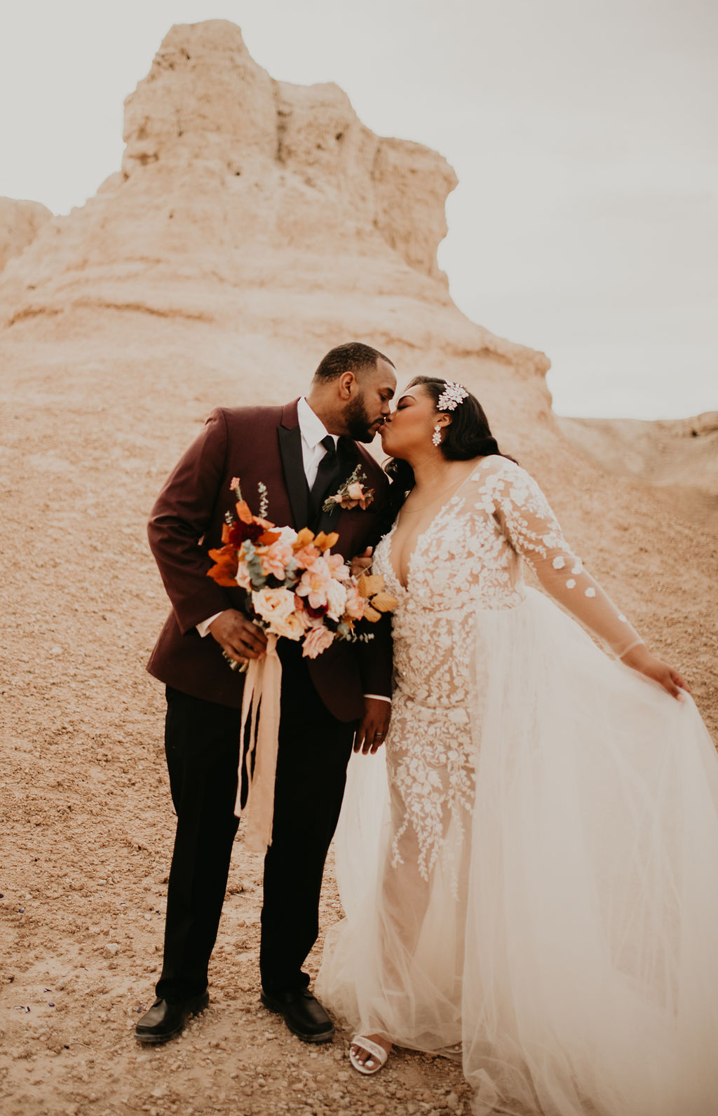 Newlyweds kissing in front of the beautiful rocks at the fossil beds as the bride takes the tule on the side of her dress and lifts it out.