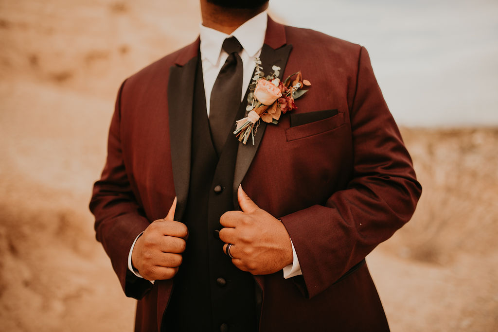 The grooms boutonniere of a blush rose and some small wild flowers on his deep red suit.  