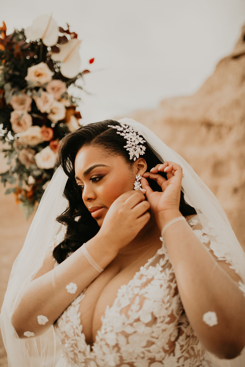 Close up photo of the bride and the beautiful details of lace on her wedding dress with a hair comb on the side of her old Hollywood style curls and a veil placed on the back. As she fixes her diamond earrings. 