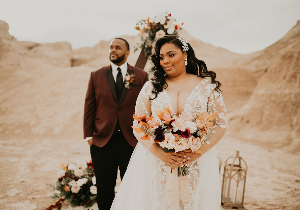 Fossil Beds Sunset Elopement. Newlyweds deep in the fossil beds of tule springs at a triangular arch for an alter with flowers, and candles on a bohemian rug