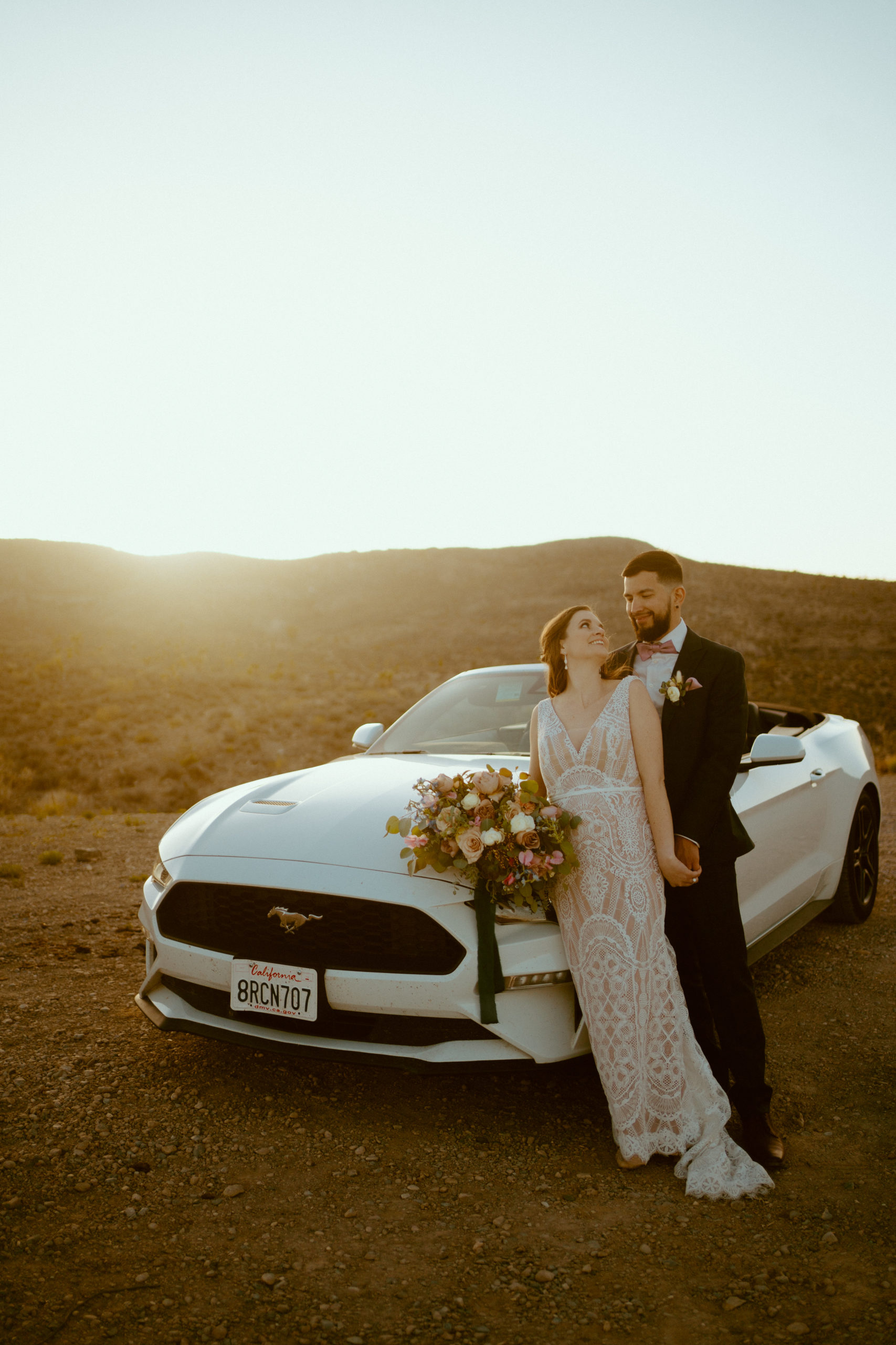 Newlyweds in the desert next to their Mustang 