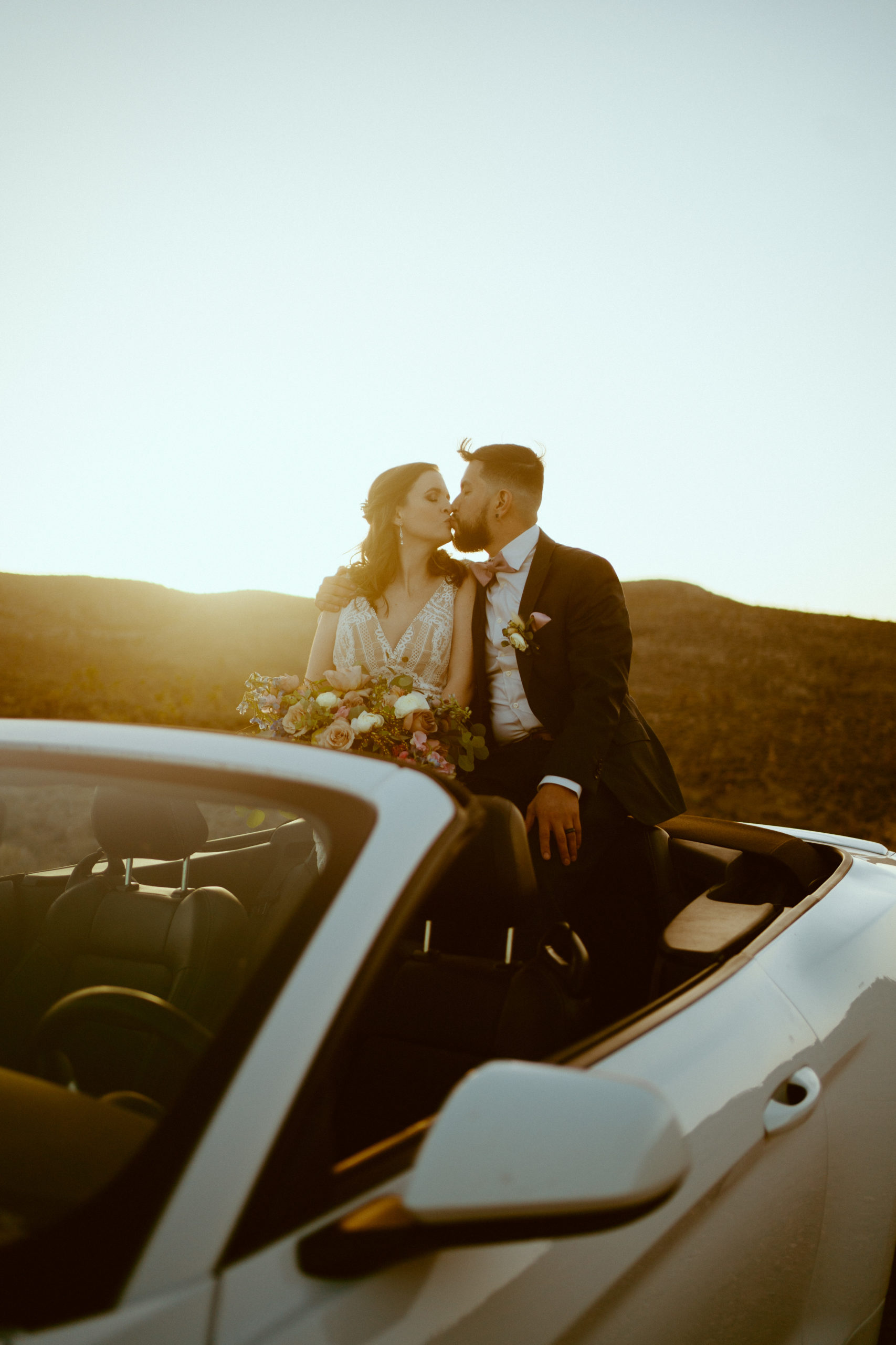 Newlyweds kissing on back of convertible Mustang 