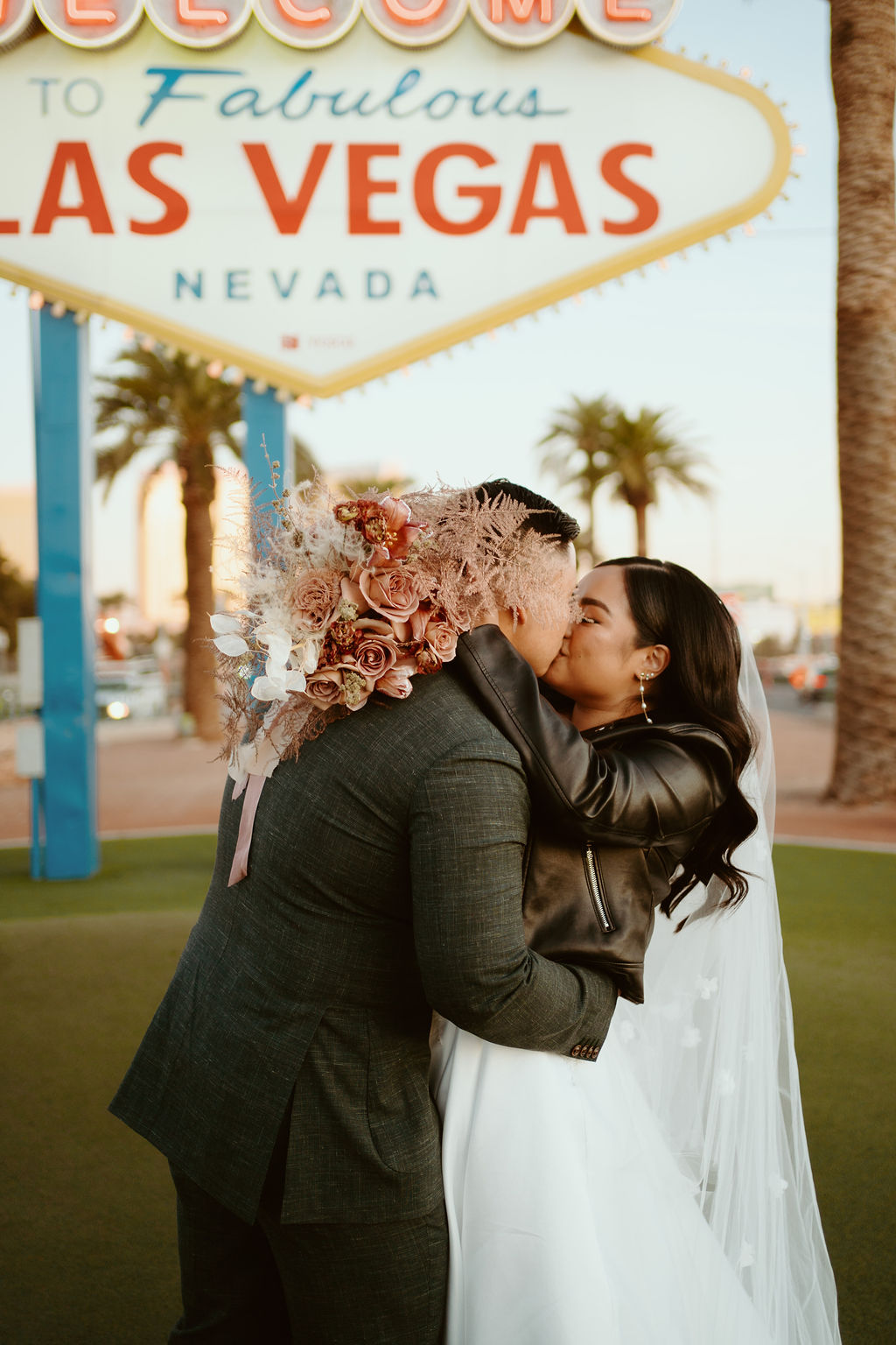 Bride with Dusty Rose bouquet and Custom Black Leather Bridal Jacket with Groom in front of Welcome to Fabulous Las Vegas Nevada Sign during Las Vegas Highlights & Desert Elopement