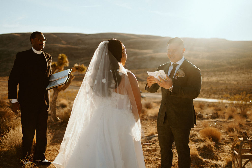 Groom reading vows to bride while sun rises behind him 