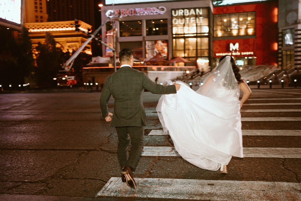 Groom holding bride's dress and walking across cross-walk on the Las Vegas Strip 