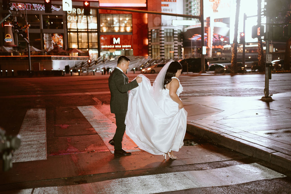 Groom holding bride's dress and walking across cross-walk on the Las Vegas Strip before Elopement 