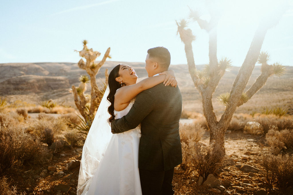 Bride laughing during first dance in desert while sun rises 