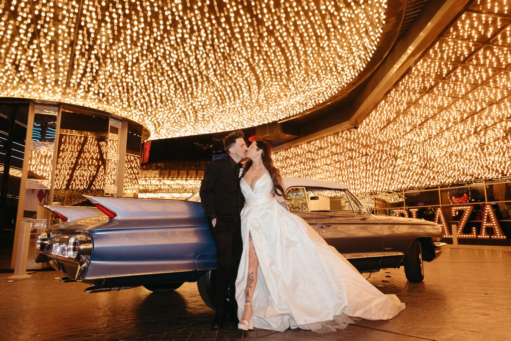 Bride and groom standing by classic car under lights in downtown las Vegas