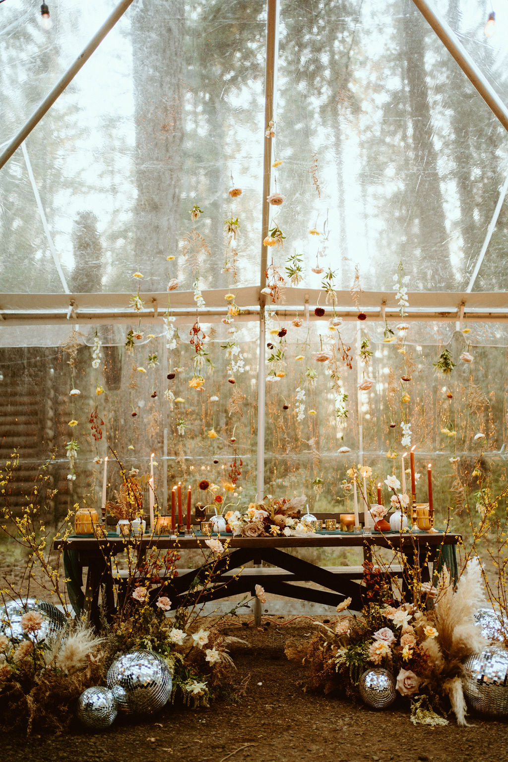 Loloma Lodge Retro Whimsical Micro-Wedding. Wooden sweetheart table with a turquoise table runner and rust and mustard taper candles lit under an assortment of dangling flowers and wild flowers, pampas and disco balls all around the front.