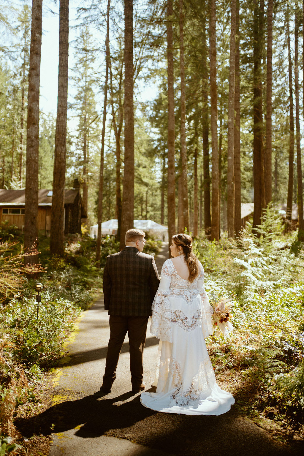 The bride and groom are holding hands walking down the road in the middle of the woods