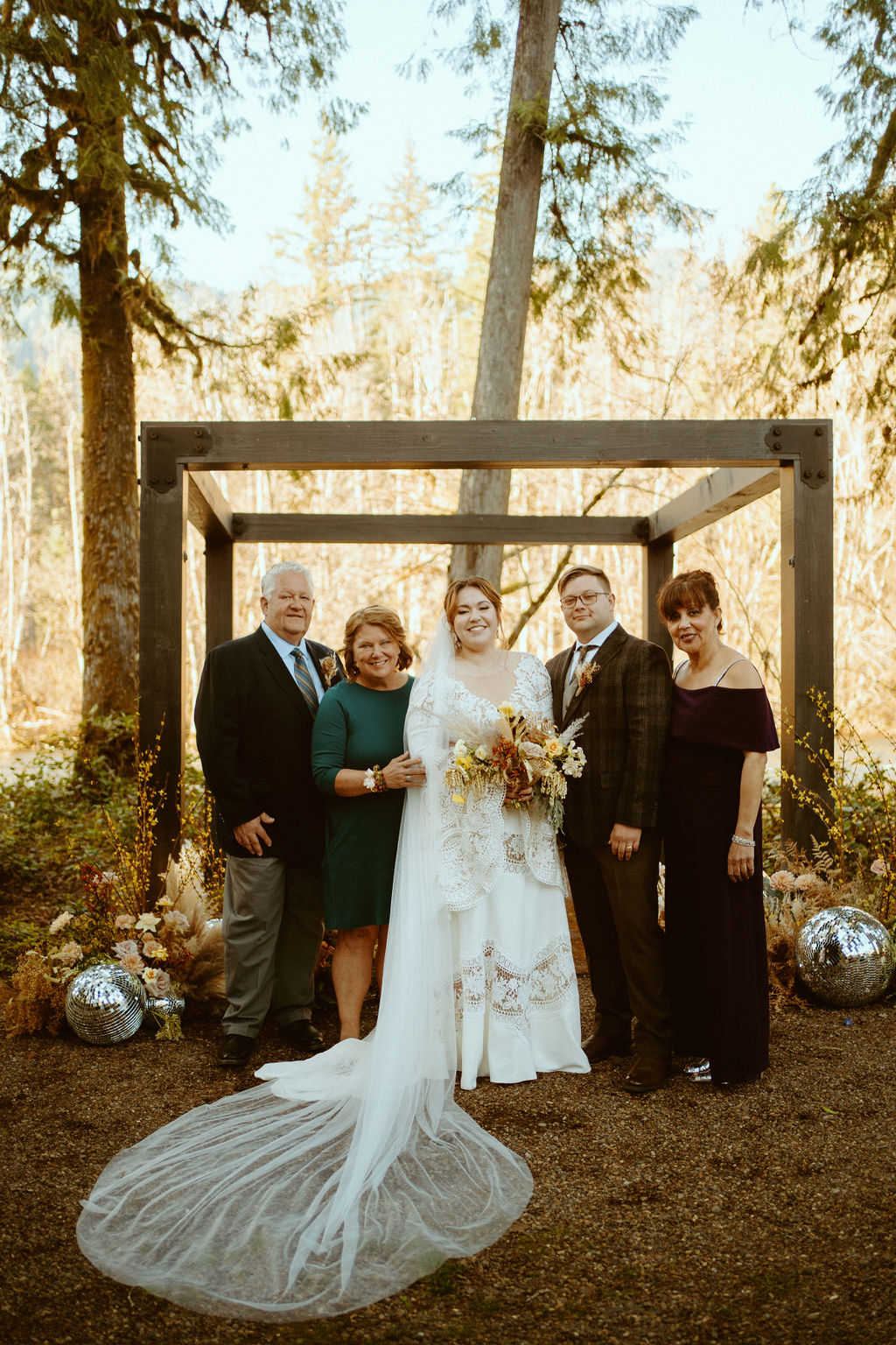 The bride and groom pose with mother and father of the bride and mother of the groom in front of the wooden arch