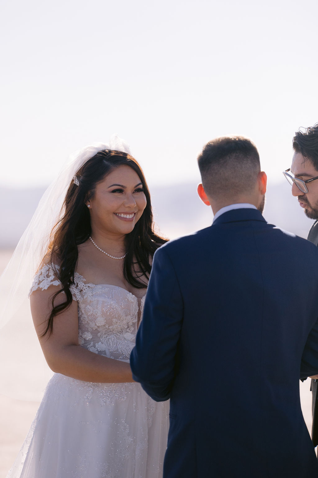 Bride stares at her groom with a wide smile as he looks over to the officiant. 